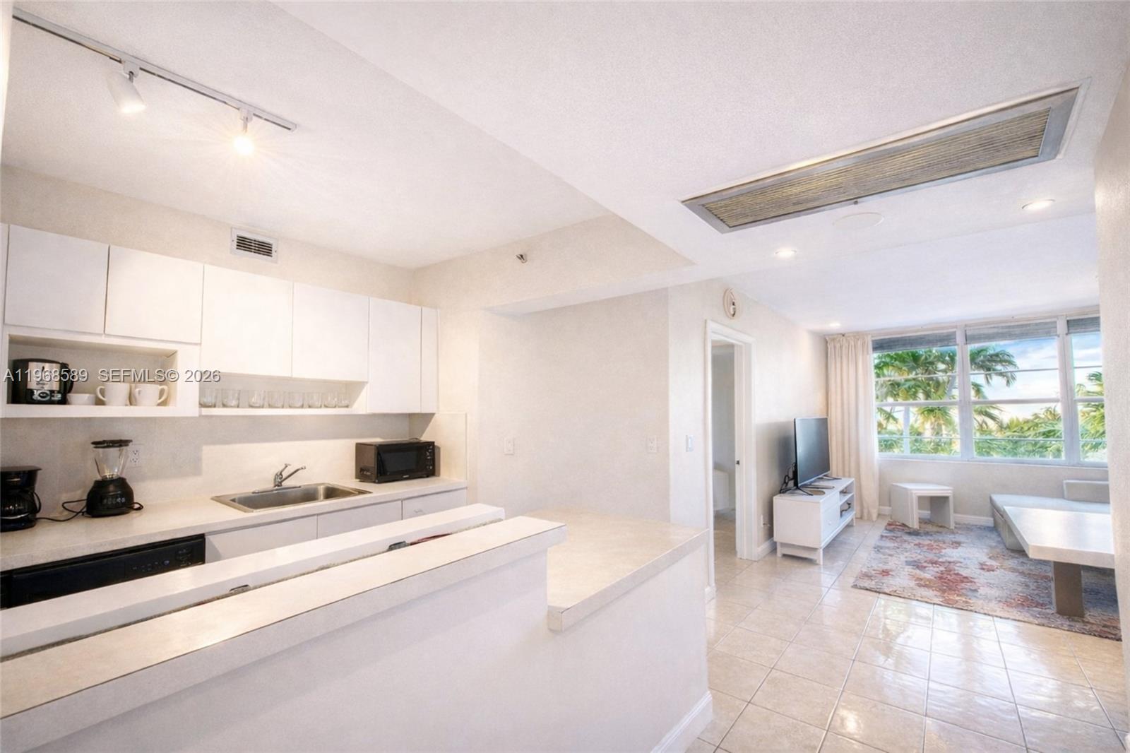 A kitchen with white cabinets and a breakfast bar opens into a living area — 100 Lincoln Rd # 415, Miami Beach FL 33139, MIAMI BEACH, FL