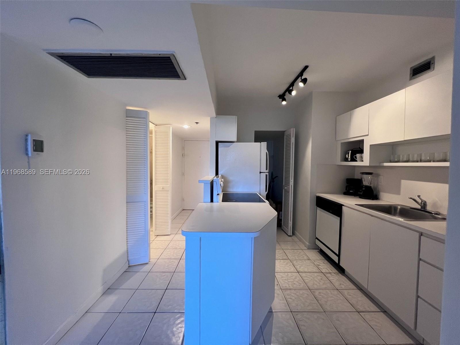 A white kitchen features tile flooring, a small island, and track lighting — 100 Lincoln Rd # 415, Miami Beach FL 33139, MIAMI BEACH, FL