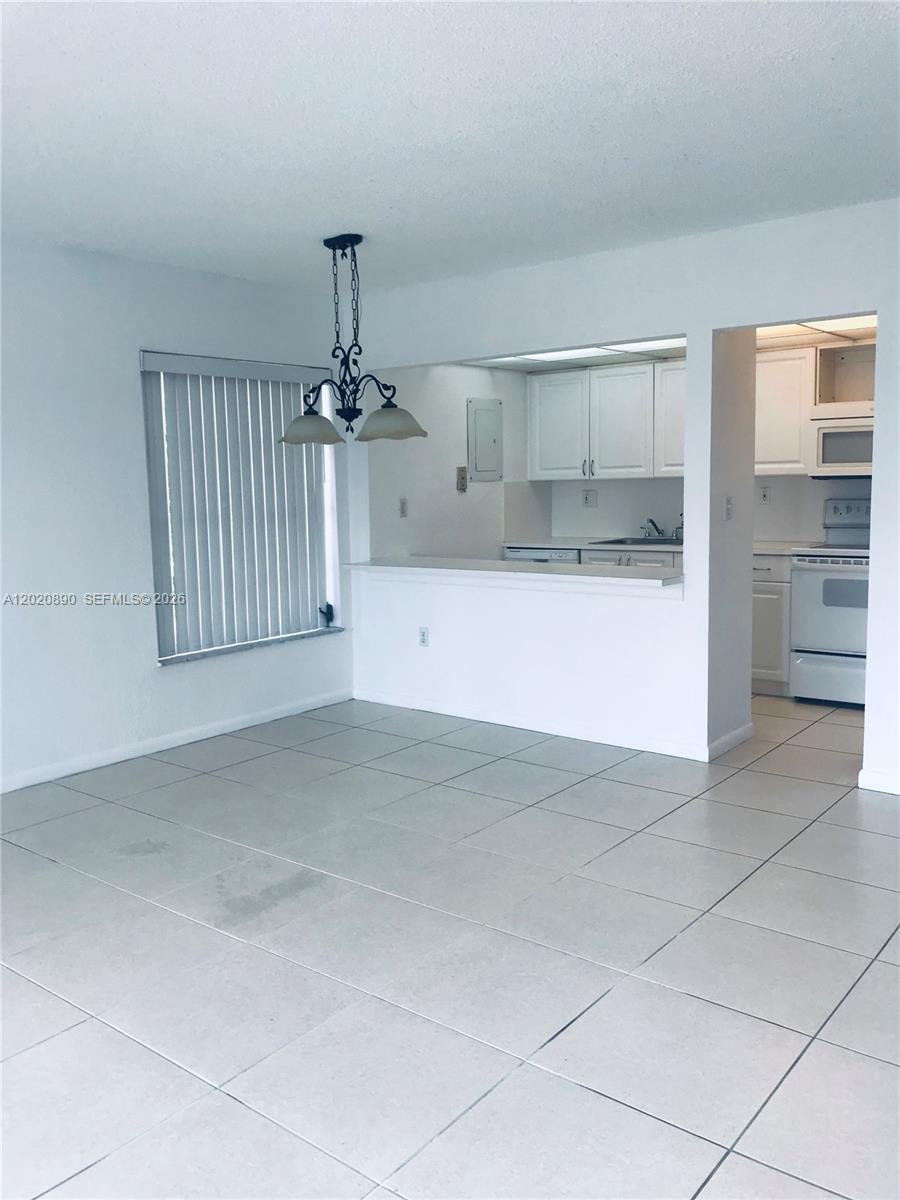 A dining area with tile floors and a pass-through window to a white kitchen — 17600 NW 68th Ave # B3006, Hialeah FL 33015, HIALEAH, FL