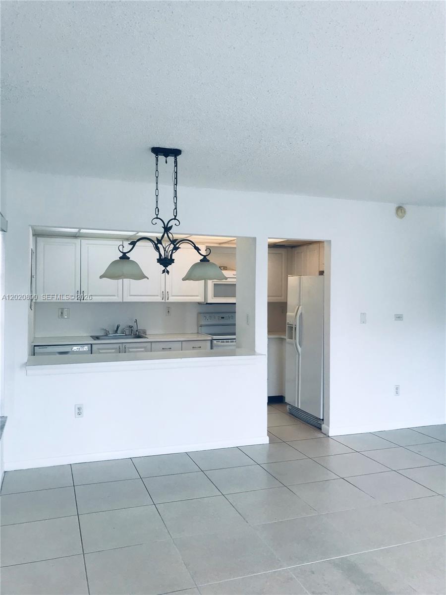 A kitchen with white cabinets and a breakfast bar overlooks a tiled dining area — 17600 NW 68th Ave # B3006, Hialeah FL 33015, HIALEAH, FL