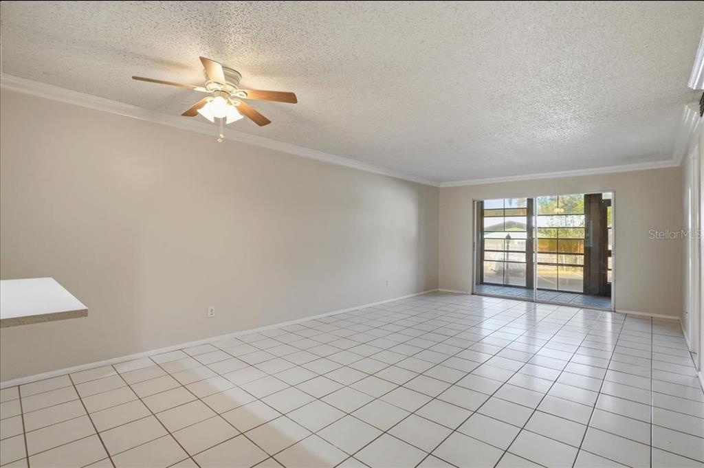An empty living room features white tile flooring, a ceiling fan, and sliding glass doors — 3700 S OSPREY AVENUE UNIT 115, SARASOTA, FL