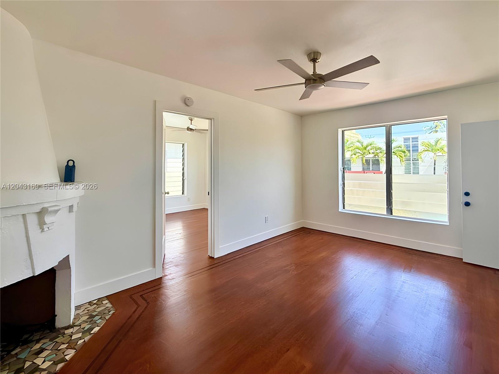 A living room features hardwood floors, a white fireplace, a ceiling fan, and a window — 641 10th St # 7, Miami Beach FL 33139, MIAMI BEACH, FL