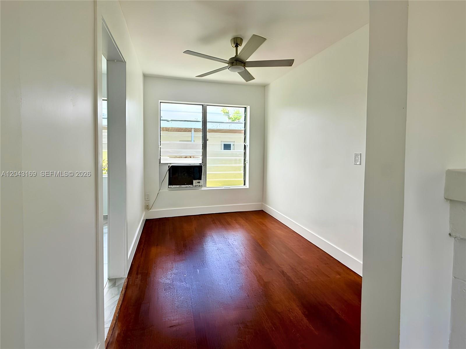 An empty room features dark hardwood flooring, white walls, a ceiling fan, and a window unit — 641 10th St # 7, Miami Beach FL 33139, MIAMI BEACH, FL