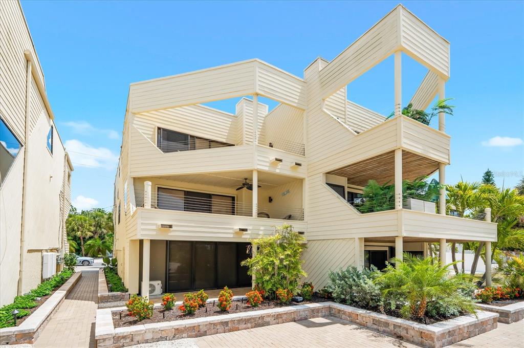 A multi-story, light-colored wooden house features multiple balconies and a landscaped front garden — 548A BEACH ROAD, SARASOTA, FL