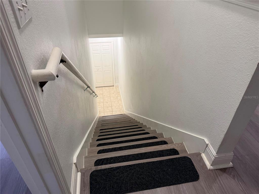 A staircase with wood-look treads and black non-slip mats leads down to a tiled landing — 1300 EASTERN PECAN PLACE UNIT 208, WINTER GARDEN, FL