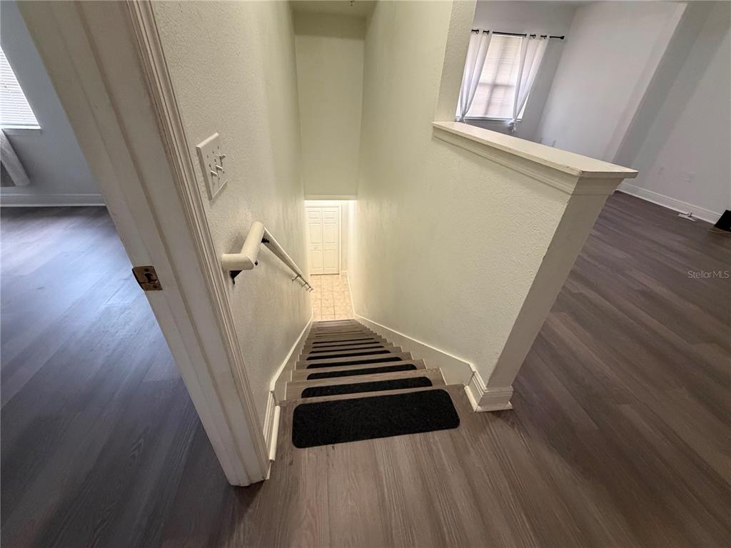A staircase with dark treads leads down to a tiled landing with a white door — 1300 EASTERN PECAN PLACE UNIT 208, WINTER GARDEN, FL