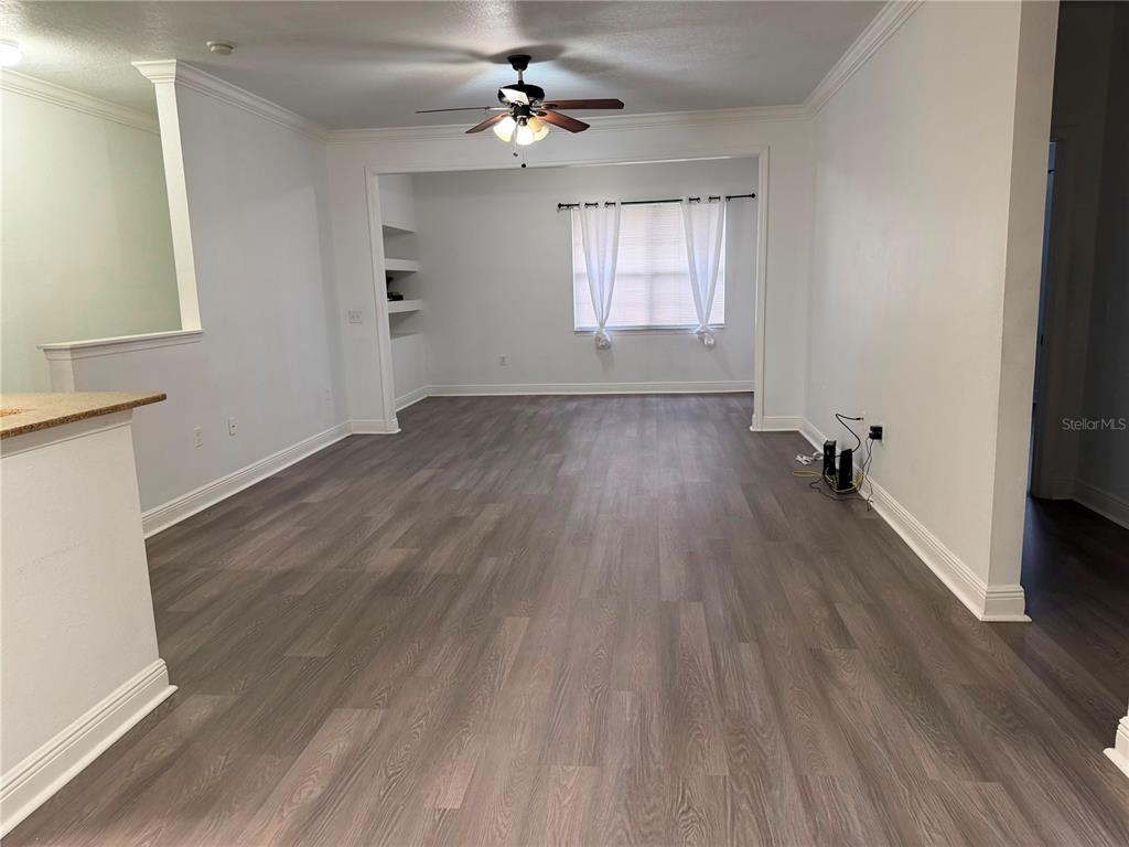 An empty living room features gray wood-look flooring, white walls, and a ceiling fan — 1300 EASTERN PECAN PLACE UNIT 208, WINTER GARDEN, FL