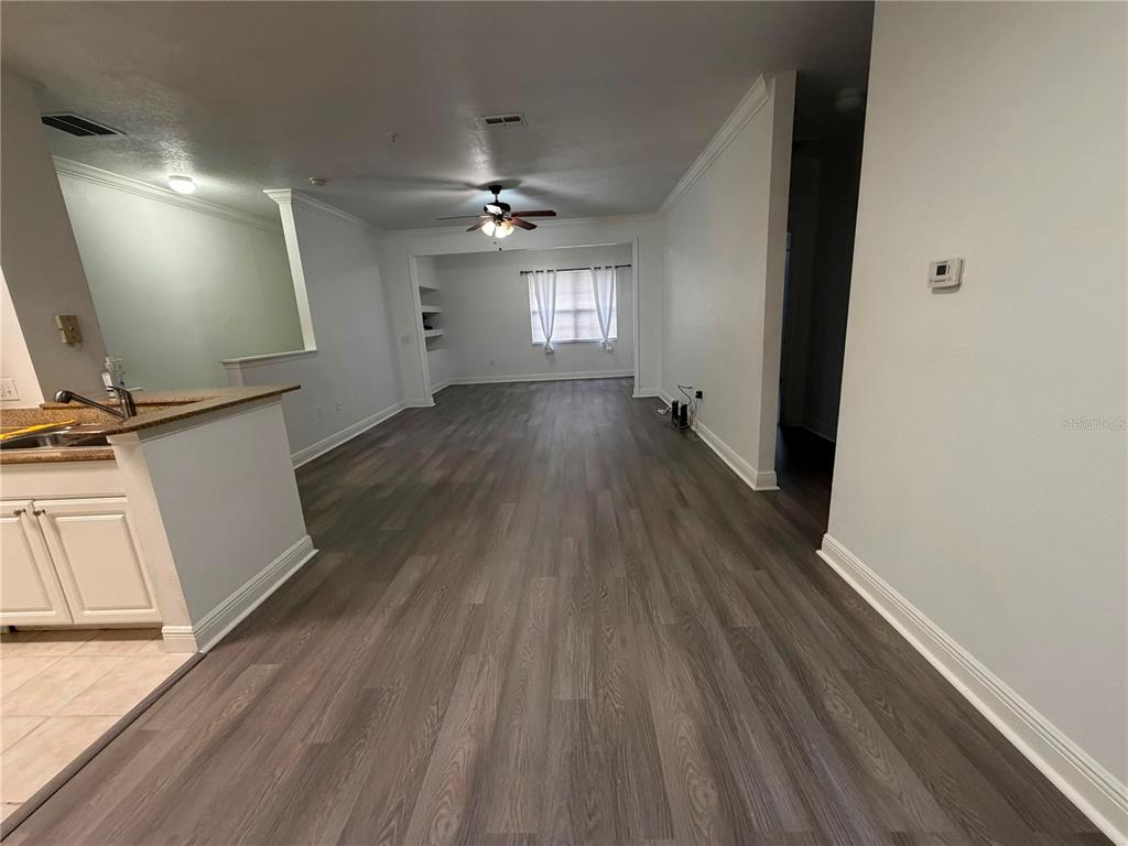 An open-concept living area features wood-look flooring, a ceiling fan, and a kitchen peninsula — 1300 EASTERN PECAN PLACE UNIT 208, WINTER GARDEN, FL