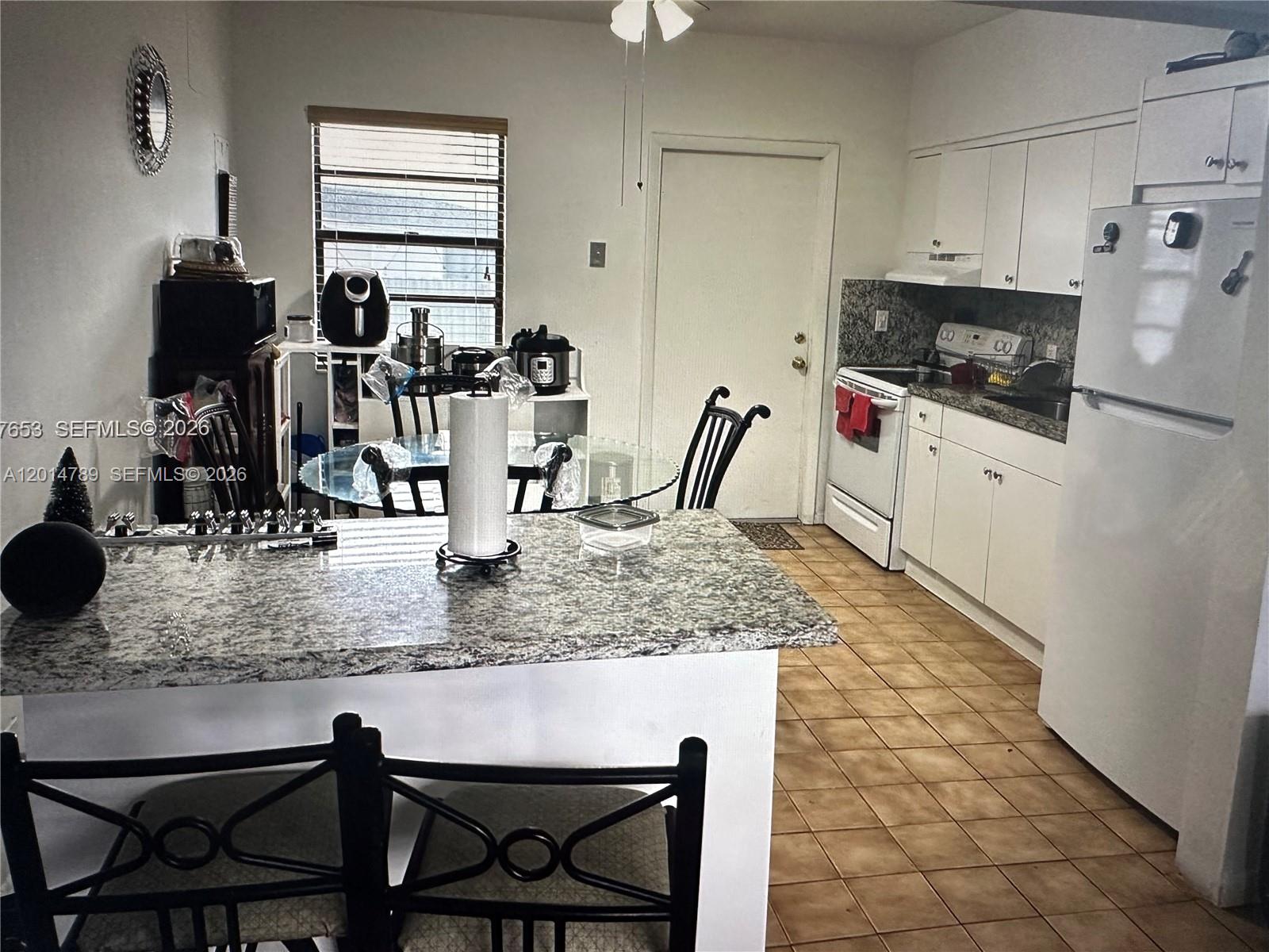 A kitchen features white cabinets, granite countertops, a white refrigerator, and a dining area — 7546 NW 2nd Ter, Miami FL 33126, MIAMI, FL