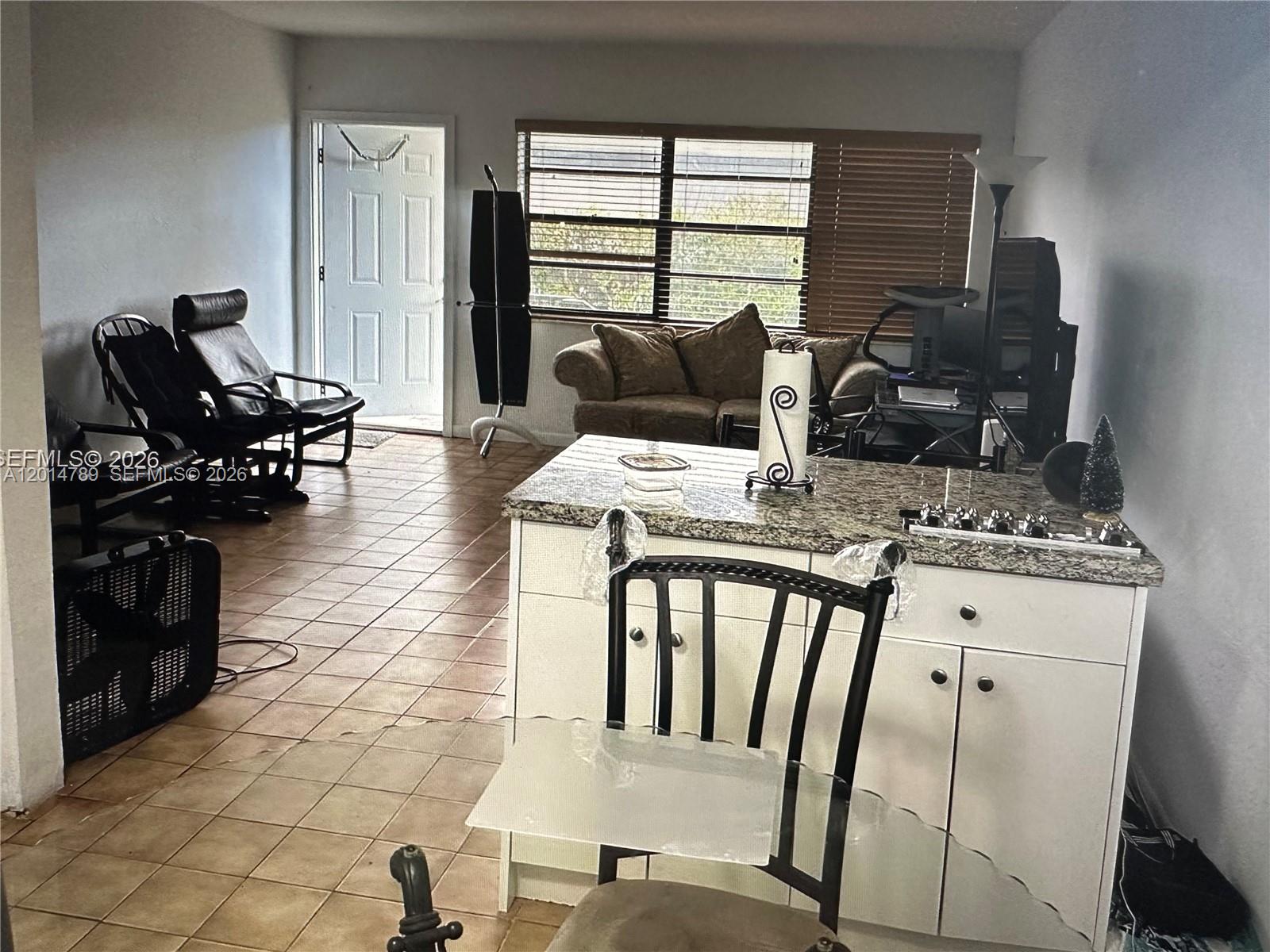 This living room and kitchen area features tile flooring, a granite-topped island, and blinds — 7546 NW 2nd Ter, Miami FL 33126, MIAMI, FL