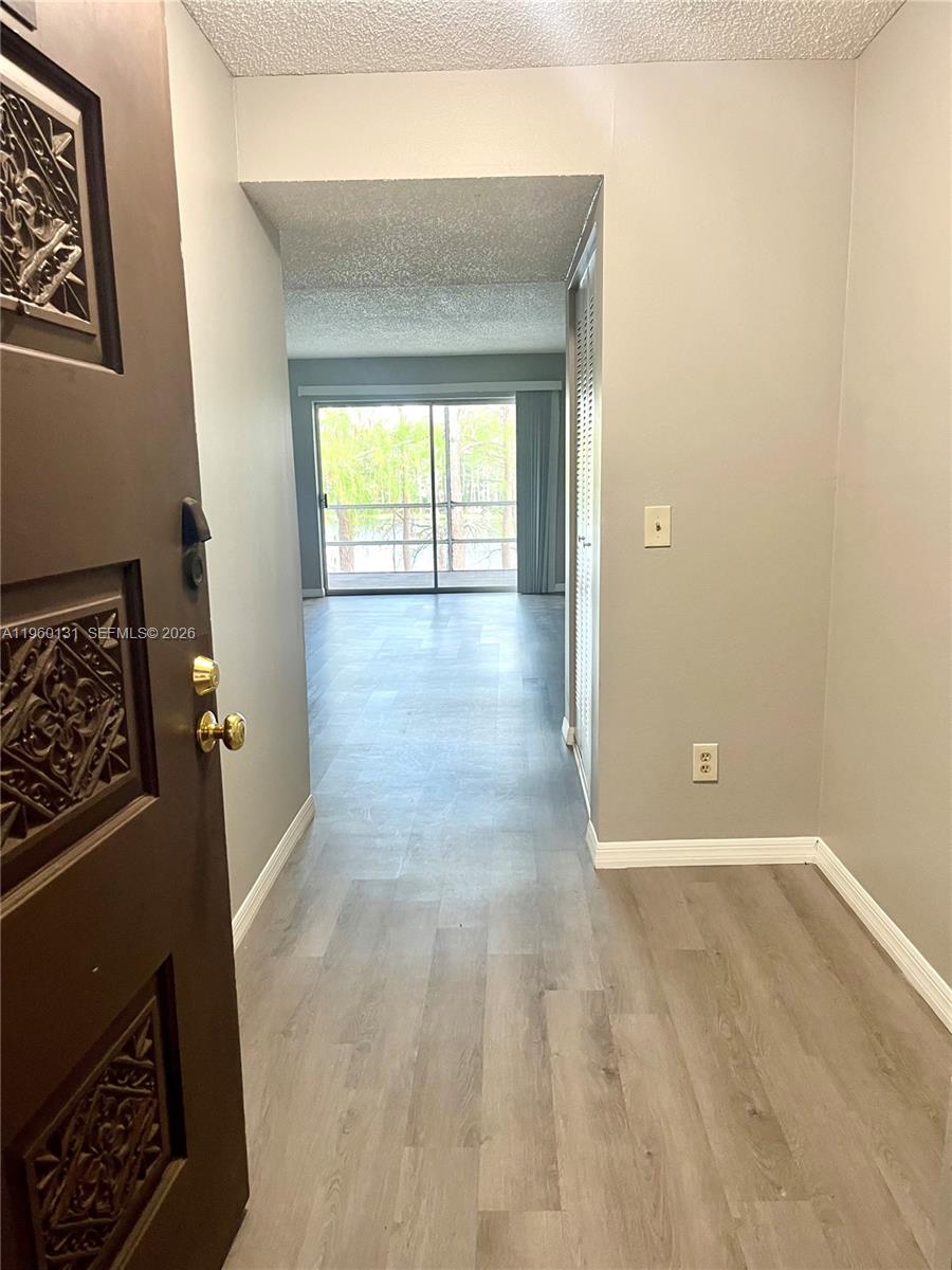 An entryway with wood-look flooring leads into a living area with a sliding glass door — 4575 S Texas Ave # 307, Orlando FL 32839, ORLANDO, FL