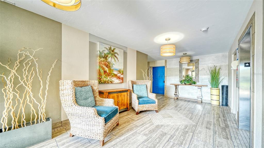 A lobby features two wicker armchairs, a wooden console table, and a bright blue door — 225 HOURGLASS WAY UNIT 106, SARASOTA, FL