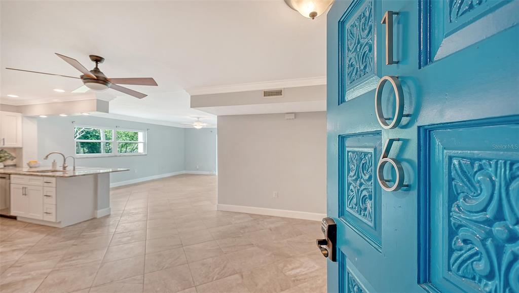A bright open-concept living area with tile floors is viewed through an open blue door — 225 HOURGLASS WAY UNIT 106, SARASOTA, FL