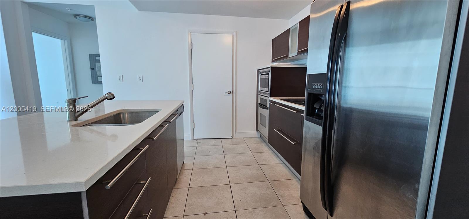 A modern kitchen features dark wood cabinetry, stainless steel appliances, and a white countertop island — 1900 N Bayshore Dr # 1617, Miami FL 33132, MIAMI, FL