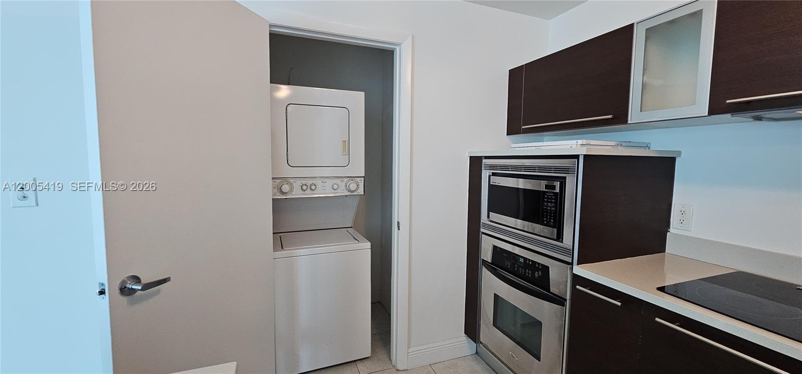 A kitchen features dark wood cabinets, stainless steel appliances, and an adjacent laundry closet — 1900 N Bayshore Dr # 1617, Miami FL 33132, MIAMI, FL