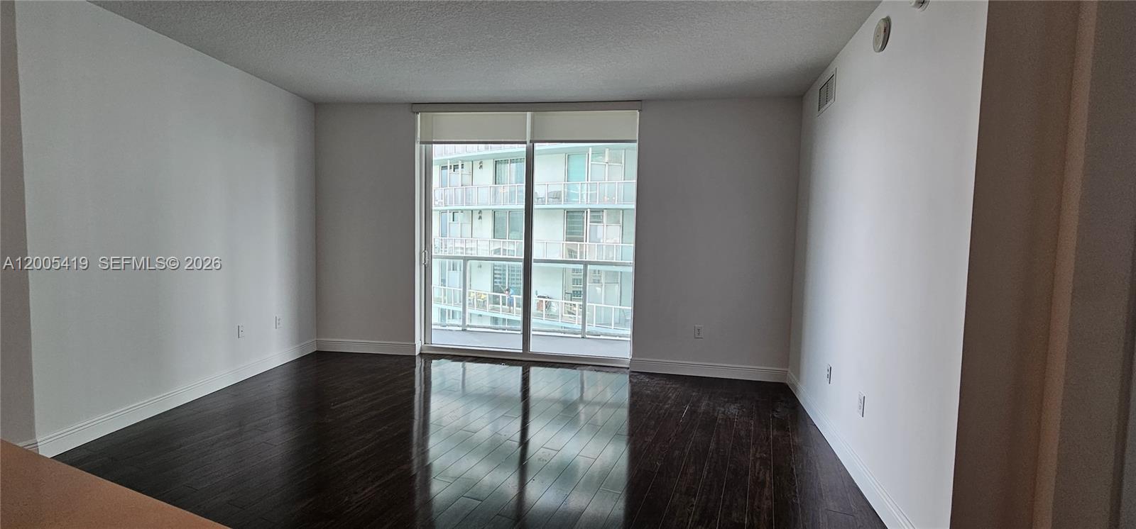 An empty room features dark hardwood flooring, white walls, and a sliding glass balcony door — 1900 N Bayshore Dr # 1617, Miami FL 33132, MIAMI, FL