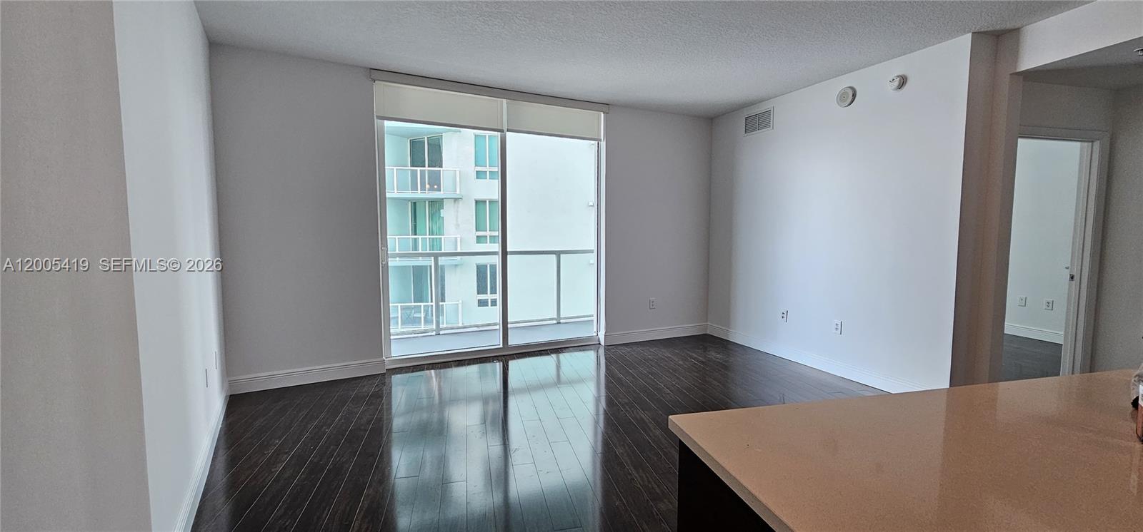 An empty room features dark wood flooring, white walls, and a sliding glass balcony door — 1900 N Bayshore Dr # 1617, Miami FL 33132, MIAMI, FL