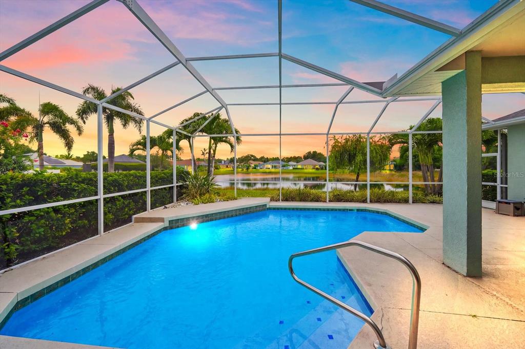 A screened-in swimming pool overlooks a lake at sunset with palm trees in the background — 12111 SUMMER MEADOW DRIVE, LAKEWOOD RANCH, FL