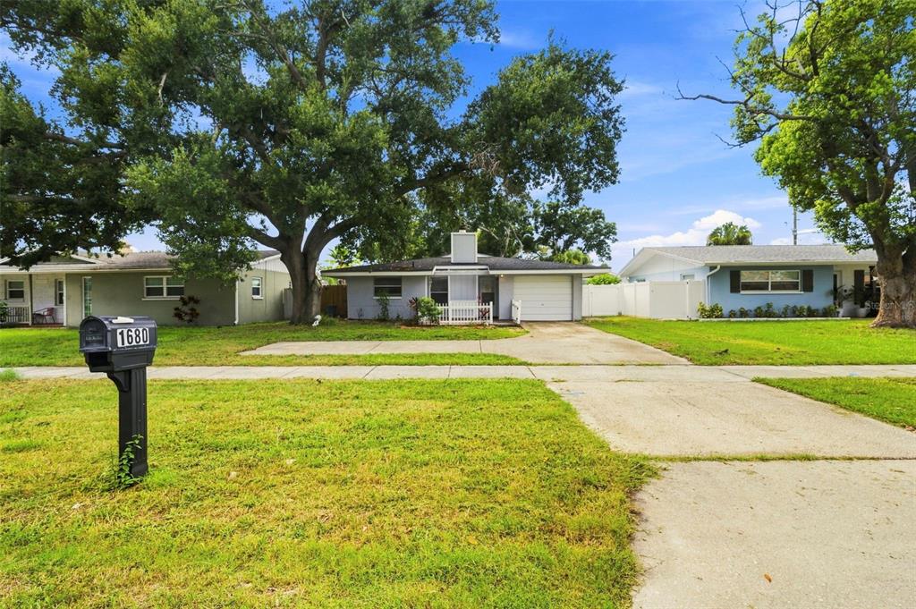 A single-story house with a concrete driveway and a large tree in the front yard — 1680 PINEHURST ROAD, DUNEDIN, FL