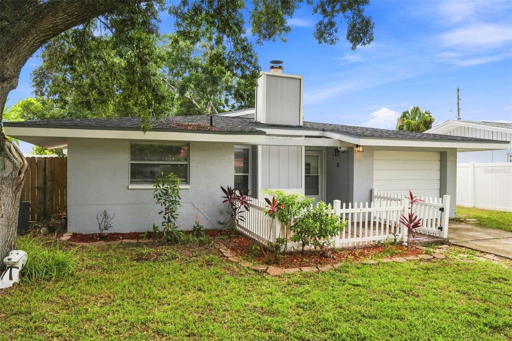 A single-story gray house with a white picket fence and a large chimney — 1680 PINEHURST ROAD, DUNEDIN, FL