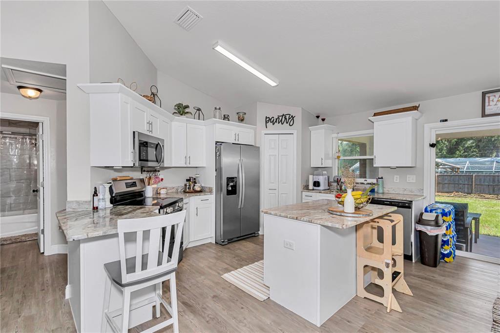 A kitchen with white cabinets, stainless steel appliances, a center island, and wood-look flooring — 3535 SE 131ST PLACE, BELLEVIEW, FL