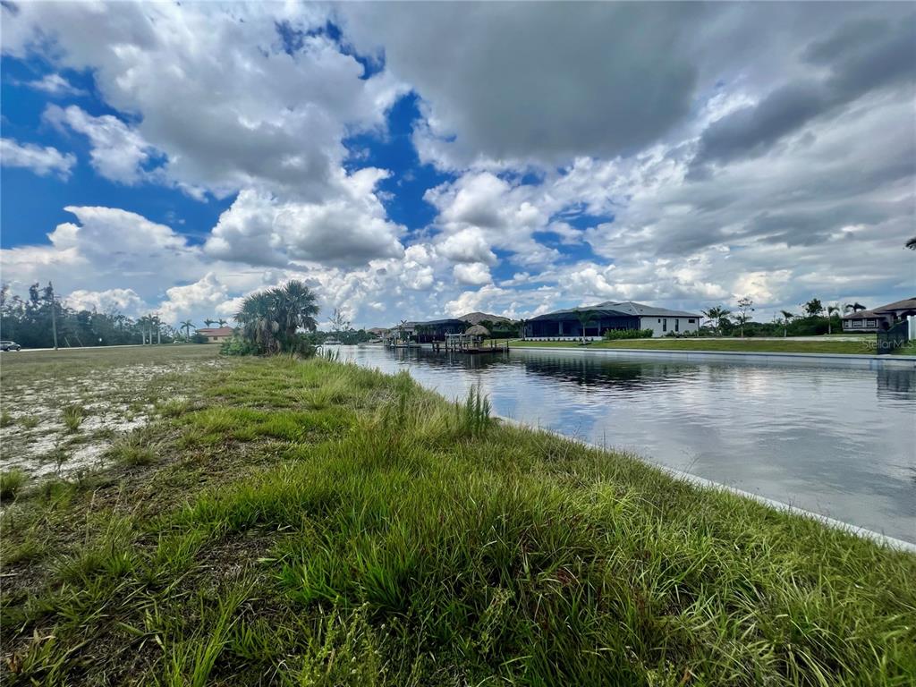 A grassy bank overlooks a canal with houses and boat docks under a cloudy sky — 2131 OLD BURNT STORE ROAD N, CAPE CORAL, FL
