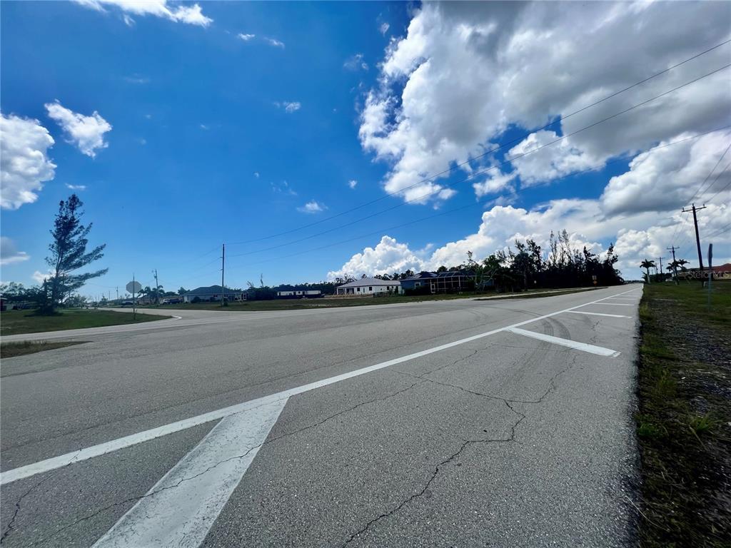 A paved road stretches toward a residential neighborhood under a bright, cloudy blue sky — 2131 OLD BURNT STORE ROAD N, CAPE CORAL, FL