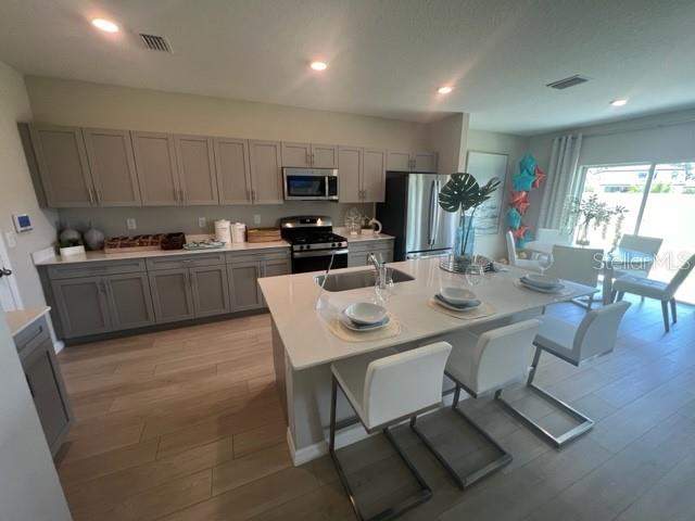 A modern kitchen features gray cabinetry, a large white island, and light wood-look flooring — 7568 HYDRANGEA LANE, WESLEY CHAPEL, FL