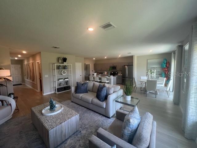 An open-concept living room features a neutral sofa, a textured coffee table, and a kitchen — 7568 HYDRANGEA LANE, WESLEY CHAPEL, FL