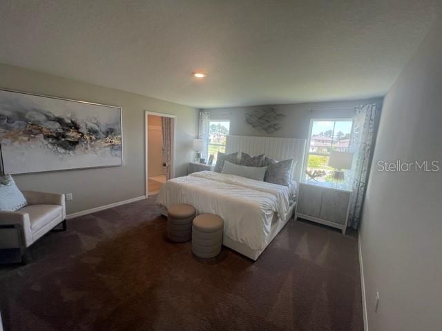 A bedroom features a large bed, a beige armchair, and a prominent abstract wall painting — 7568 HYDRANGEA LANE, WESLEY CHAPEL, FL