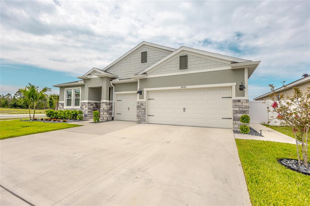A single-story house with a three-car garage, stone accents, and light gray siding — 2843 ELIO HAMMOCK DRIVE, ST CLOUD, FL