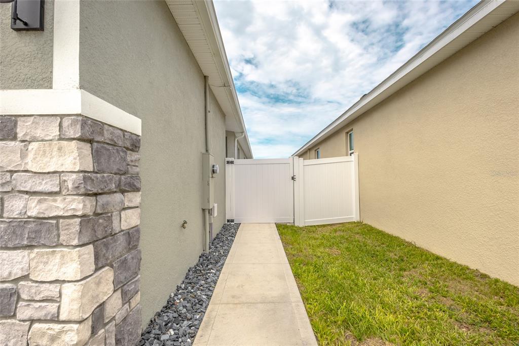 A concrete walkway leads to a white vinyl gate between two residential house exterior walls — 2843 ELIO HAMMOCK DRIVE, ST CLOUD, FL
