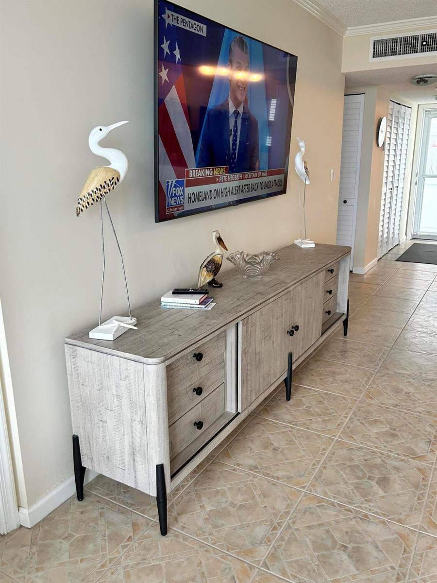 A light wood media console with black legs sits below a wall-mounted television in a room — 1391 S Ocean Boulevard, Pompano Beach FL 33062, POMPANO BEACH, FL