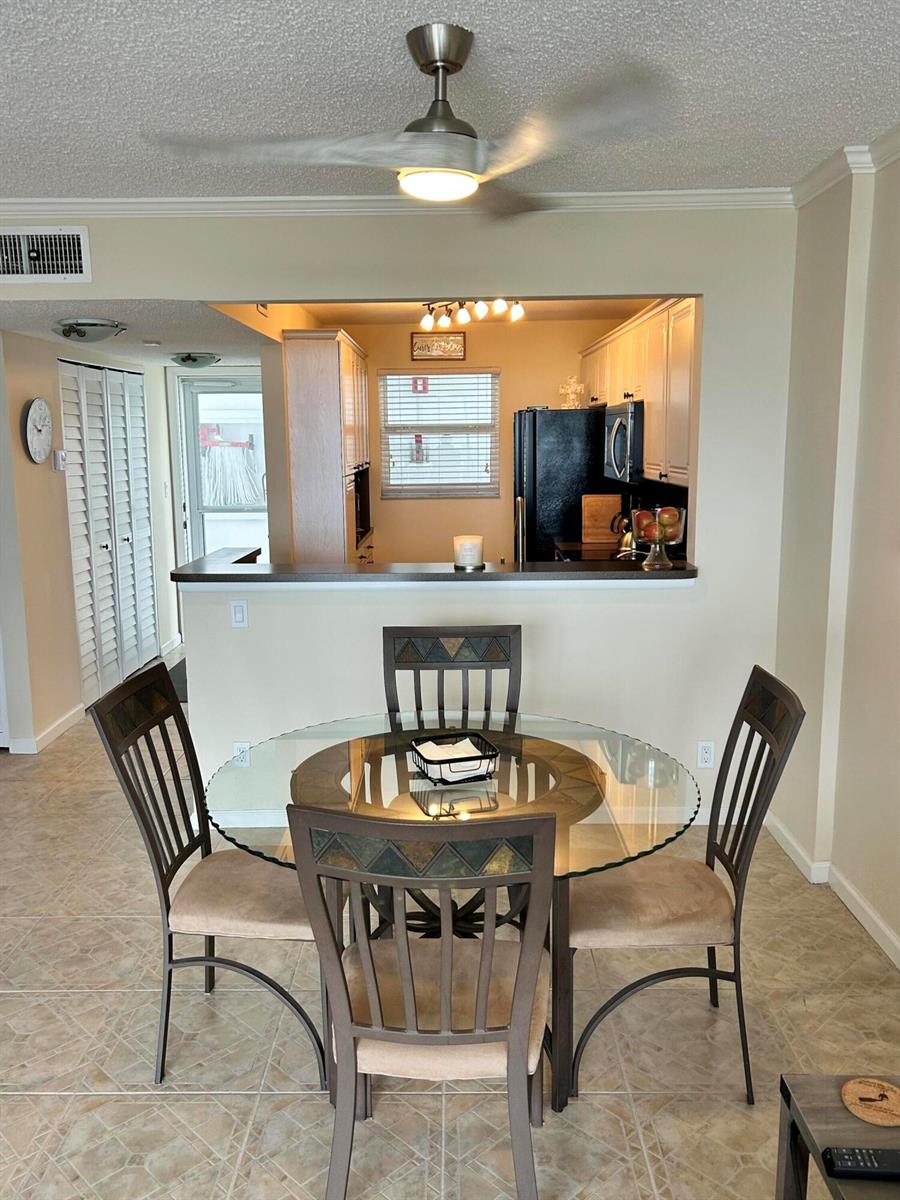 A dining area with a glass-topped table and four chairs sits before an open kitchen — 1391 S Ocean Boulevard, Pompano Beach FL 33062, POMPANO BEACH, FL