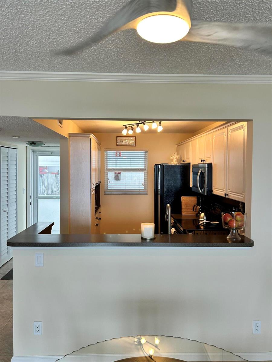 A kitchen with white cabinets, black appliances, and a breakfast bar overlooks a dining area — 1391 S Ocean Boulevard, Pompano Beach FL 33062, POMPANO BEACH, FL