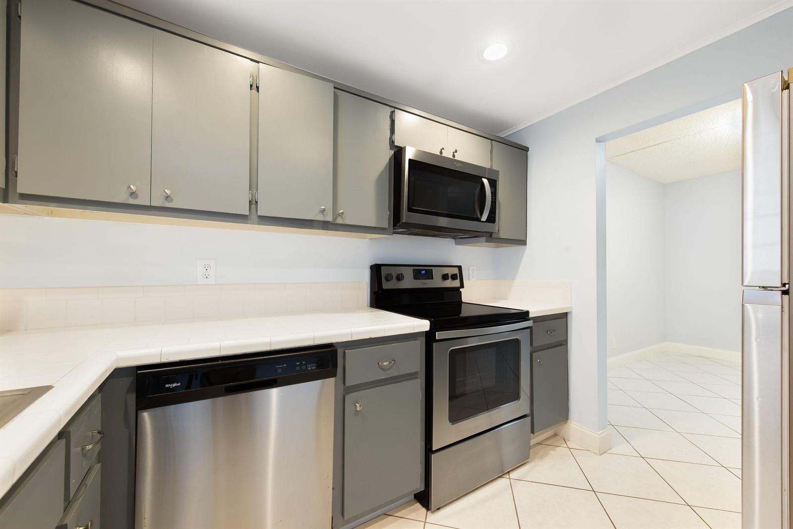 A kitchen features gray cabinets, stainless steel appliances, and white tile countertops and flooring — 1340 NE 28th Avenue # 232, Pompano Beach FL 33062, POMPANO BEACH, FL