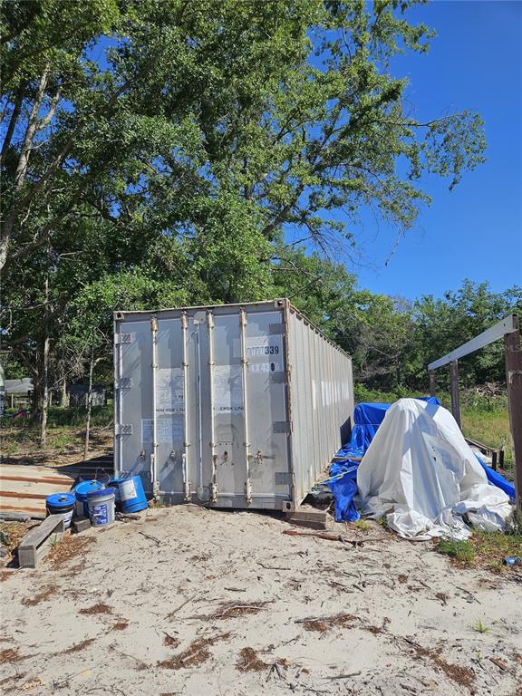 A metal shipping container sits on a sandy lot beneath large trees — 000 SW MIXSON ROAD, LAKE CITY, FL