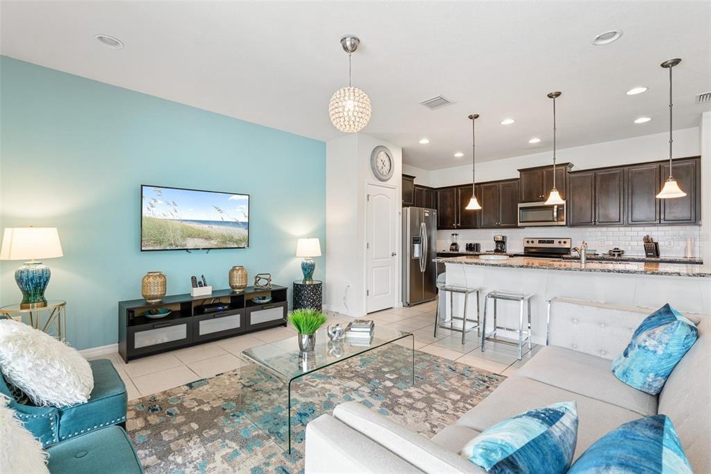 An open-concept living room and kitchen featuring a light blue accent wall and tile flooring — 8936 SYDNEY AVENUE, KISSIMMEE, FL
