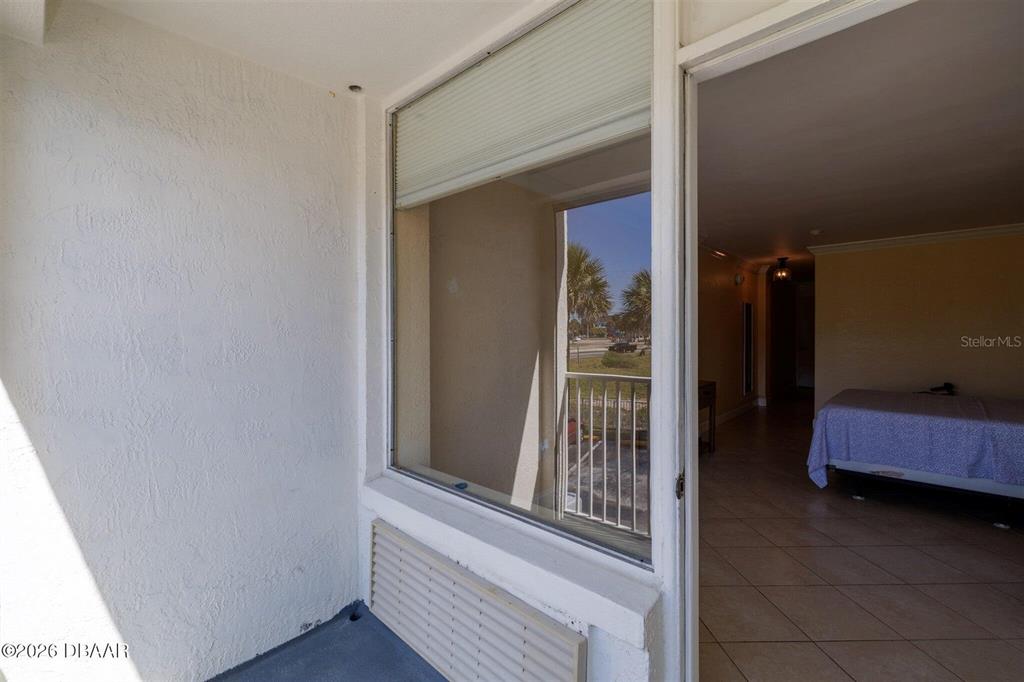 A balcony with a white wall and a window looking into a bedroom — 935 S ATLANTIC AVENUE UNIT 203, DAYTONA BEACH, FL