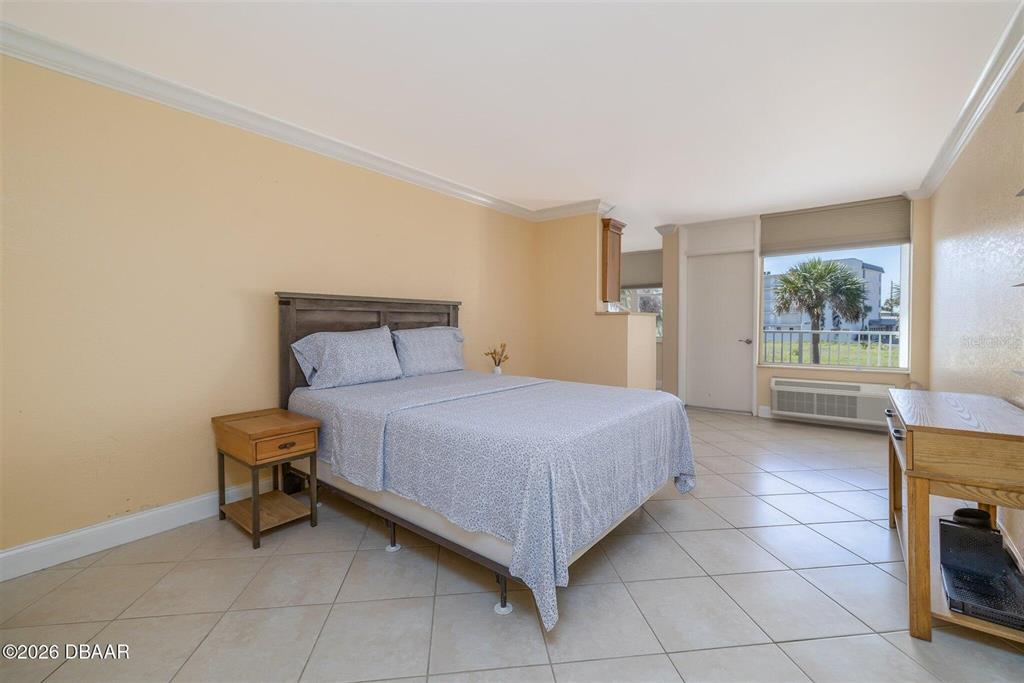 A bedroom features a bed, a nightstand, a wooden desk, and a window with balcony access — 935 S ATLANTIC AVENUE UNIT 203, DAYTONA BEACH, FL