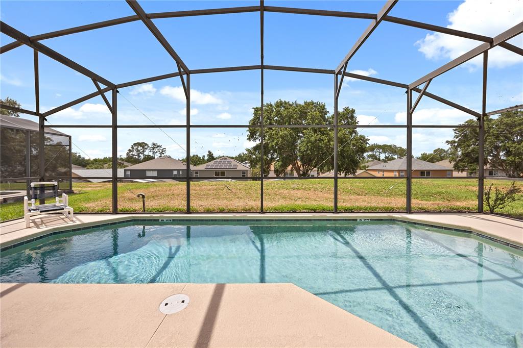 A screened-in swimming pool overlooks a grassy backyard and neighboring houses under a blue sky — 8675 LA ISLA DRIVE, KISSIMMEE, FL