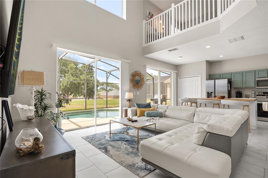 A spacious living room with a white sectional sofa, tile floors, and a view of a pool — 8675 LA ISLA DRIVE, KISSIMMEE, FL