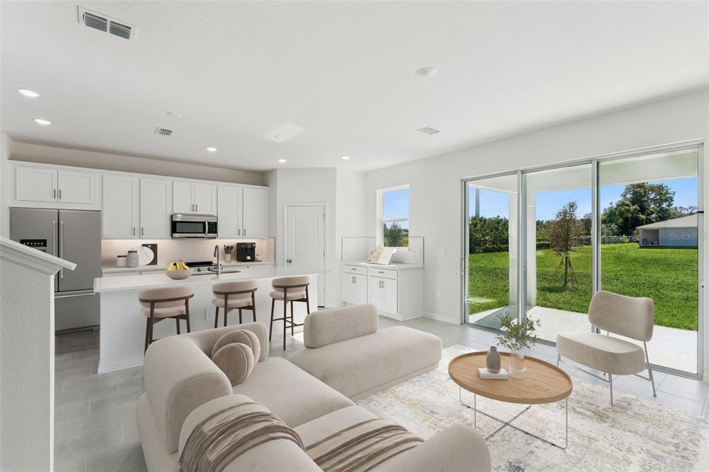 A bright, open-concept kitchen and living area featuring white cabinetry, a kitchen island, and sliding doors — 2345 HUANIER COURT, APOPKA, FL