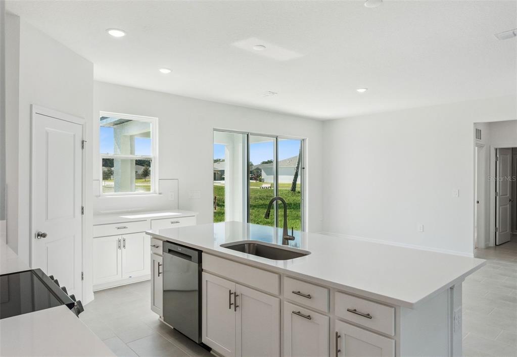 A modern kitchen features white cabinets, a large island with a sink, and sliding glass doors — 2345 HUANIER COURT, APOPKA, FL