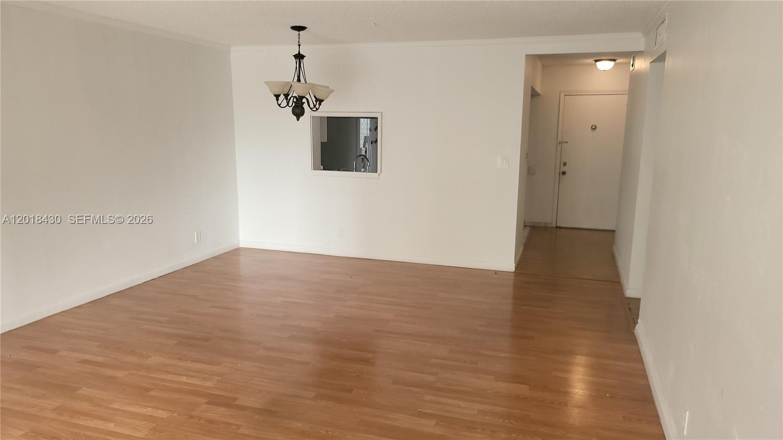 An empty room features light wood-look flooring, white walls, and a hanging chandelier — 1001 NE 14th Ave # 201, Hallandale Beach FL 33009, HALLANDALE BEACH, FL