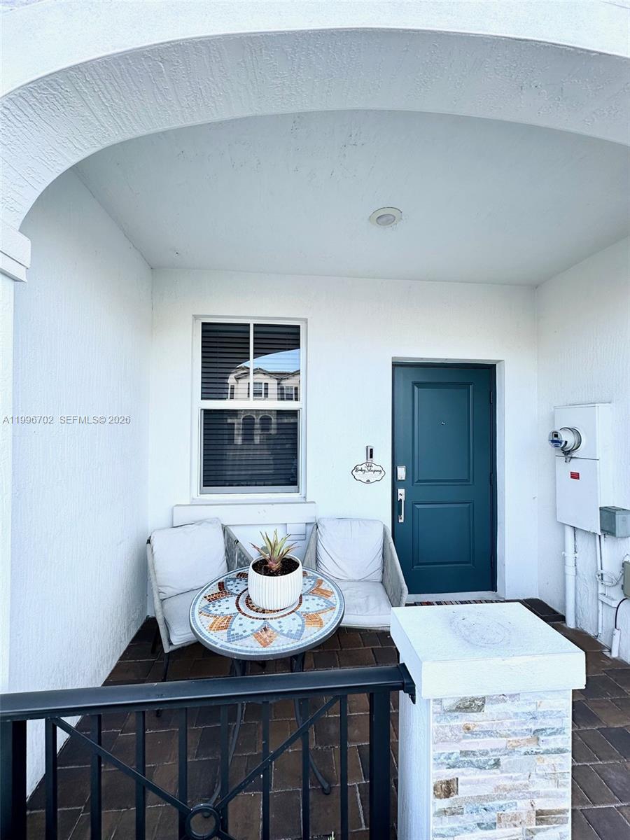 A covered front porch features a small mosaic table, two chairs, and a dark door — 12774 NW 23rd Pl, Miami FL 33167, MIAMI, FL