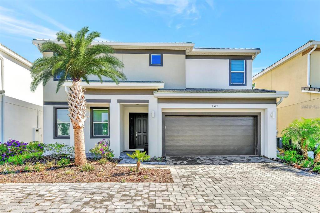 A two-story house with a gray garage, a palm tree, and a paved driveway — 2547 SHANTI DRIVE, KISSIMMEE, FL