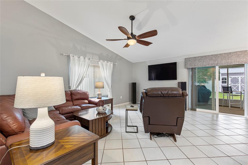 A living room features a brown leather sofa, a recliner, tile flooring, and a ceiling fan — 102 EASTWOOD DRIVE, PALM COAST, FL