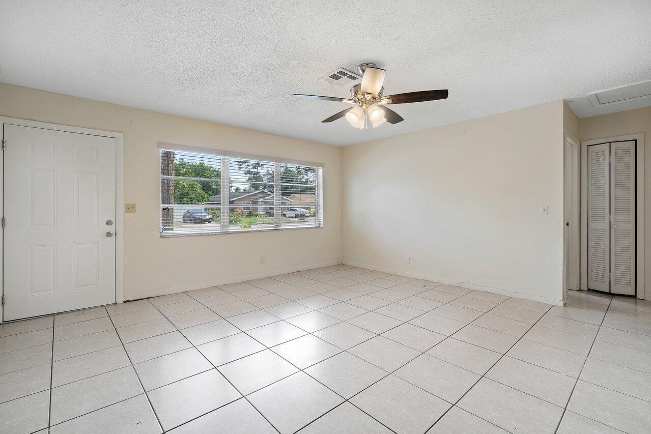 An empty room with light-colored floor tiles, a ceiling fan, and a large window — 5854 Kumquat Road # A, FL 33413, FL