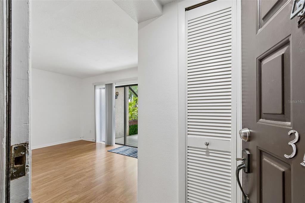 An entryway with wood-look flooring leads to a living area with a sliding glass door — 2971 ESTANCIA BOULEVARD UNIT 313, CLEARWATER, FL